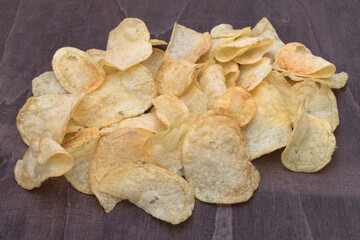 Pile of crispy potato chips on wooden surface