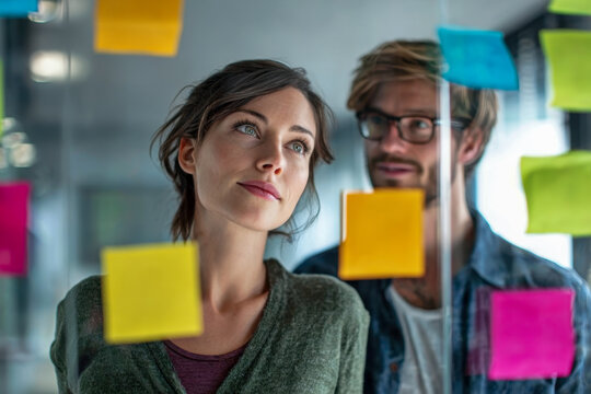 Young professionals brainstorming creative ideas in a modern office surrounded by colorful notes on a glass board during a collaborative planning session - Powered by Adobe