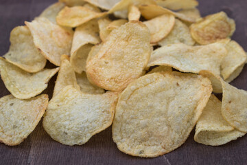 Pile of crispy potato chips on wooden surface