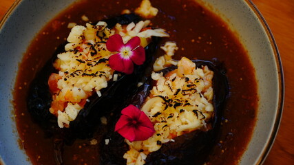 Platillo gourmet con chiles rellenos bañados en salsa roja, con camarón y decorados con pétalos comestibles.