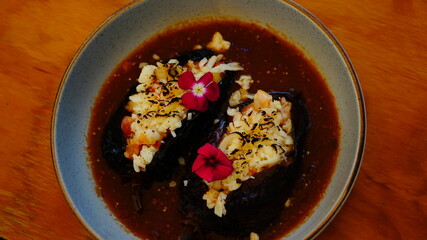 Platillo gourmet con chiles rellenos bañados en salsa roja, con camarón y decorados con pétalos comestibles.