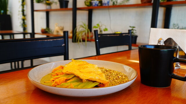 Platillo servido en plato artesanal con una omelette dorada acompa&ntilde;ada de flor de calabaza y salsa verde.