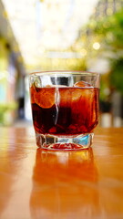 vaso corto con bebida oscura y rodajas de limon spbre una mesa de madera
