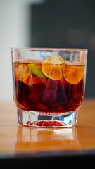 vaso corto con bebida oscura y rodajas de limon spbre una mesa de madera