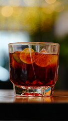 vaso corto con bebida oscura y rodajas de limon spbre una mesa de madera