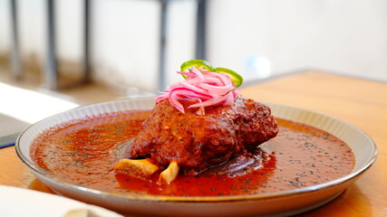 Platillo tradicional mexicano bañado en salsa roja, decorado con cebolla morada encurtida y rodajas de chile verde.