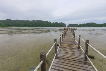 Fototapeta premium Wooden bridge spans a body of water, with a few boats visible in the distance