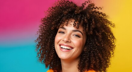 Close-up portrait of happy young woman with voluminous curly hair smiling against vibrant multicolor pink, blue, and yellow background, beauty and diversity concept