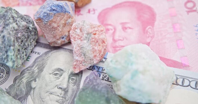 Raw mineral stones on US and China currency. Represents rare-earth mining, supply chain rivalry, commodity markets, and strategic mineral investment trends.