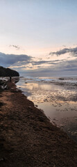 Spring landscape. Panoramic view of beautiful dawn on bay. Cumulus clouds over water in bright light. Ice, snow and rocks on coastline. Rising rays of sun are reflected in sea. Vertical photo.
