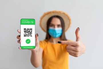 Individual displays a digital COVID-19 vaccination passport on their smartphone, wearing a face mask and a hat, in a bright indoor environment.