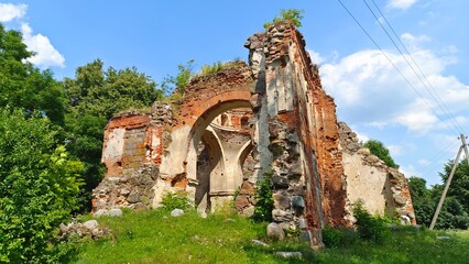 Naklejka premium On a grassy hillock there are the remains of a church destroyed during the First World War, previously built of stone and red brick. There is a power line nearby. Sunny summer weather and blue sky