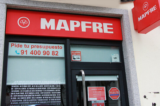 R&oacute;tulo Mapfre seguros, letrero con logotipo en fachada y puerta de entrada a oficina con cartel de aseguradora global espa&ntilde;ola l&iacute;der en Espa&ntilde;a