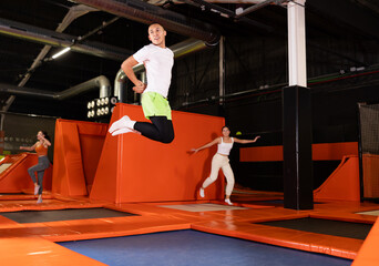 Cheerful young man in sportswear enjoying high jump, surrounded by bright colorful setting of modern indoor trampoline park ..