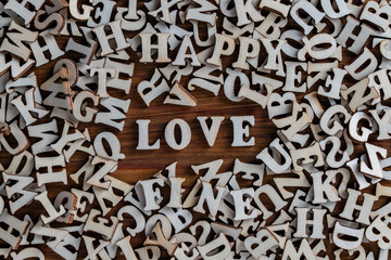 Pile of wooden letters of the English alphabet, laid out in a chaotic order and the word love in the center on a table, closeup, top view. Background of many wooden letters