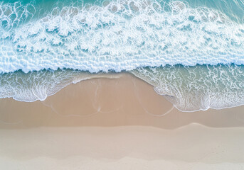 Aerial view of ocean waves washing onto a sandy beach on a sunny day. The turquoise water creates a beautiful contrast with the golden sand, perfect for travel and vacation themes