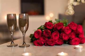 A cozy indoor setting features a bouquet of red roses and two elegant wine glasses arranged on a table. This scene captures the essence of love and romance for Valentine's Day.