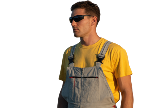 Man in sunglasses, yellow t-shirt, and gray overalls looking left, illuminated by warm sunlight against a transparent background. background removed - Powered by Adobe