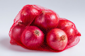 A fresh bundle of red onions contained in a vibrant red mesh bag resting on a clean white surface with soft natural lighting highlighting the glossy skins