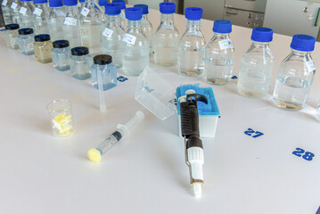 Laboratory storage bottles, plastic bottles, pipette, syringe and filters on white table.