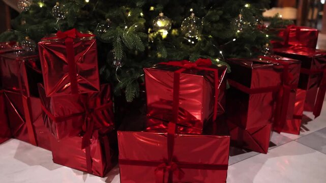 red presents, decorative gifts, Christmas spirit. Shiny red presents with ribbons arranged beneath Christmas tree adorned with string lights and transparent ornaments in festive setting.