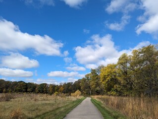 country road in the autumn; White bright clouds against a fall colored blue sky lead into this prairie walk lined by trees. Simple and beautiful. 