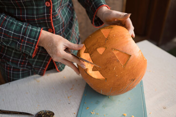 Hands of woman carving big orange pumpkin into jack-o-lantern for Halloween, close up