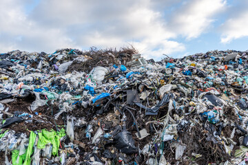 Mountains of waste fill a landfill in a rural area under a cloudy sky during mid-afternoon
