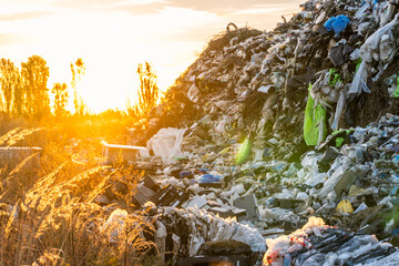 Sunset over a large landfill site with heaps of trash and waste in the foreground and glowing sunlight in the background