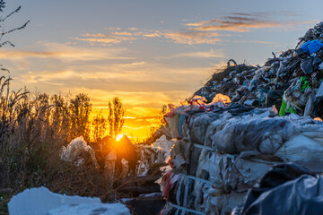 Sunset over a garbage dump with scattered plastic waste and trees in the background