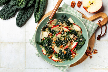 Kale, quinoa, apple and pecan salad in a green plate. Healthy vegan meal, white table surface, copy...
