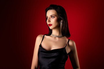 Naklejka premium Gentle young woman in a black dress with glamorous jewelry on a red gradient background exuding beauty and confidence