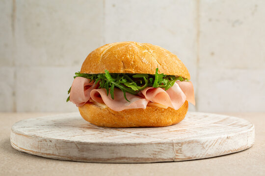 Mortadella sandwich with cheese and arugula on a white wooden board.