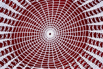 White crochet doily in circular geometric pattern placed on red background. Concept of handmade art, vintage style, traditional style. Craft background