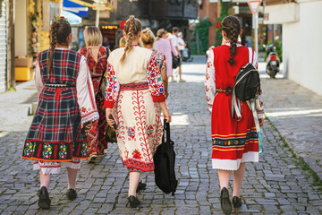 Women wearing traditional Bulgarian folk costumes walking on cobbled street during cultural event. Concept of heritage, folklore and national identity