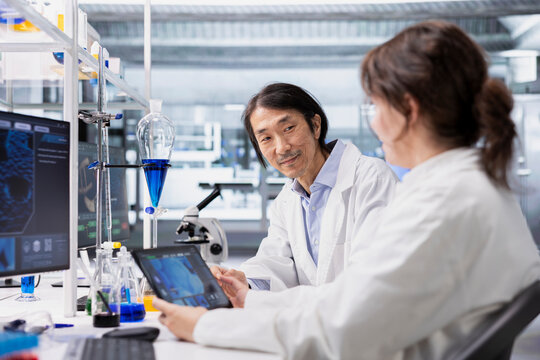 Smiling laboratory scientists using tablet app to process DNA patient data for clinical research. Upbeat lab colleagues use touchscreen device to do lab genetic analysis diagnostics