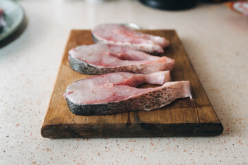 Large, freshly sliced pieces of cleaned silver carp lie on a cutting board on the table. The concept is for preparing a fresh and healthy fish dish.