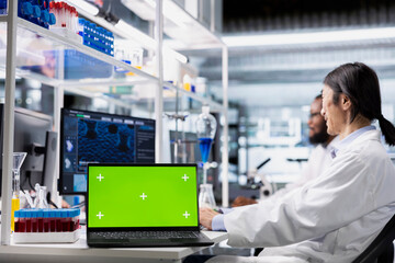 Green screen laptop used by senior researcher in laboratory to process DNA patient data for clinical research. Asian employee uses mockup notebook to do lab genetic analysis diagnostics