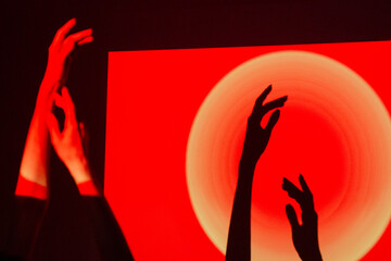 Shadows of hands interact with vibrant light patterns in a creative art display during the evening hours