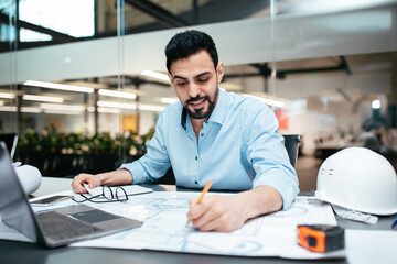 A man is focused on creating detailed technical plans at a desk in a contemporary office. He is...