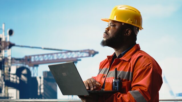 African american worker on offshore platform deck configuring derrick management systems for more efficient oil extraction. Drilling rig ship expert doing seabed analysis using laptop