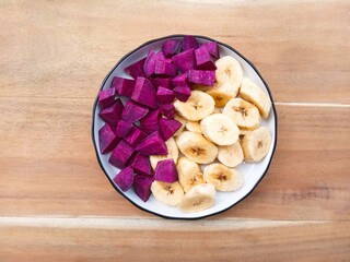 A plate filled with pieces of banana and purple sweet potato on a wooden background. Healthy meal. Ingredients for healthy food