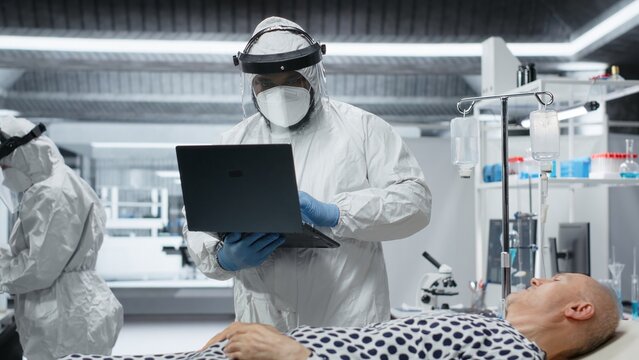 Medic in protective coveralls and gloves treats a patient in quarantine, analyzing infection data and testing vaccines to prevent outbreak spread and improve healthcare crisis. Camera B. - Powered by Adobe