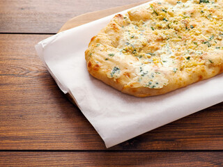 Flat sour dough bread with four cheeses on cooking paper and wooden table. Simple food. Italian style dish with high quality ingredients, Bakery product.