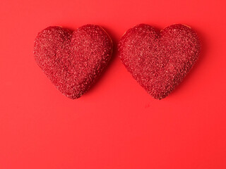 Two heart shaped doughnuts on red color surface. Top of the product is covered with colored sweet icing. Food for a Valentine day or special romantic event. Creative bakery product.