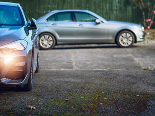 Two cars parked in a back yard of a country house. Cost of living out of the city in rural area. Expense of running two cars in a family theme. Need for transportation.