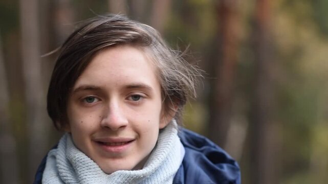 Portrait of a smiling 13-year-old teenage boy in a jacket with a scarf in an autumn park	
