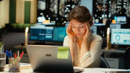 Business director sleepy and burdened at the office late at night, experiencing workplace challenges and anxiety. Discouraged woman struggling with intense workload after hours. Camera A.
