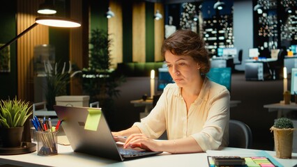 Businesswoman documenting essential ideas from pc screen on paper, planning and scheduling tasks late at night. Notetaking with handwriting for presentation that reflects objectives. Camera A.