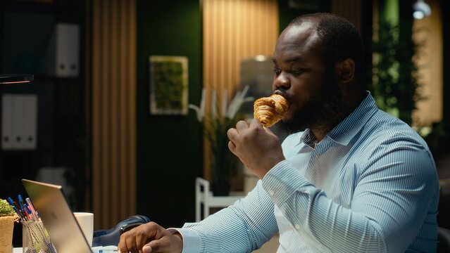African american professional overeating and working late at night, serving unhealthy food and dealing with a compulsive eating disorder due to overtime and constant tension. Mental health. - Powered by Adobe